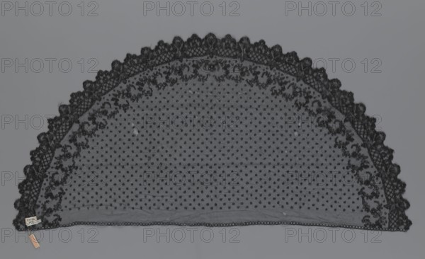 Veil; creator, veil; lace; clothing accessory; fashion. Lace with a floral-geometric pattern running in a wide strip along the semicircular, serrated edge. The remaining part features fond de Tulle and regularly spaced small circles. 19th century, France. Clothing. Height 35 cm, width 74 cm., A semicircular piece of lace fabric with a scalloped outer edge and an inner border of floral lace sits against a gray background; the lace is black with a dotted mesh pattern filling the central area and ornate embroidered floral motifs along the curved edge, and there is a small rectangular tag attached near one end with a short strip dangling from it; visible colors are black, gray, and a small area of beige on the dangling strip.