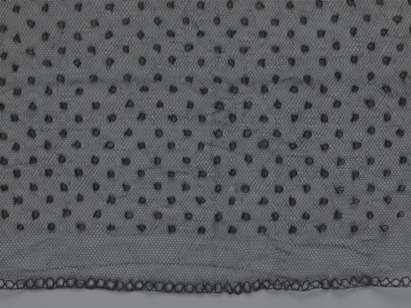 Veil;, lace; clothing accessory; ; fashion. Lace with a floral-geometric pattern running in a wide strip along the semicircular, serrated edge. The remaining part features fond de Tulle and regularly spaced small circles. 19th century, France. Clothing. Height 35 cm, width 74 cm., A piece of sheer fabric with a fine hexagonal mesh pattern in shades of dark gray and black, dotted with a scattered pattern of small raised tufts in black, and a decorative scalloped trim along one edge showing interlinked loops in black against a slightly lighter gray background.