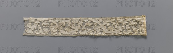 Two fragments of appliqués on batiste tulle: a with a floral tendril pattern; b with a fragment of cardboard sewn on. 19th century, Europe; lace and embroidery appliqué patterns; clothing accessory fabric; width 5.5 cm, length 34 cm., A narrow horizontal strip of lace with a floral and leafy pattern laid against a smooth background, showing a delicate net-like ground with raised embroidered motifs in off-white and cream tones, with areas of pale yellowing and light beige along the edges; the lace has irregular edges and slight fraying, and a few small loose threads cast soft shadows on the gray background.