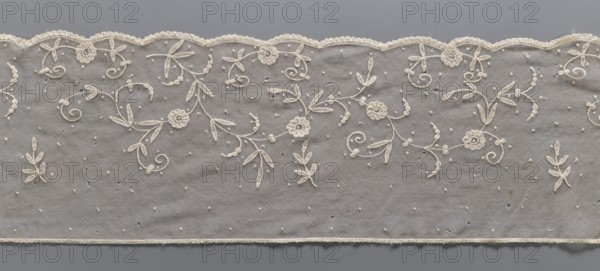 Lace fragment, lace, plant ornaments. The lower edge is gently serrated with flat arches, bordered with a band of fine, bobbin-shaped teeth, looped onto the mesh. Ornament elements made with chain and bobbin-shaped techniques. Bobbin-shaped mesh, hand-made. 2nd half of the 19th century, Europe. Lace, width 26.5 cm, length 283 cm., A strip of delicate net fabric with an ornate scalloped edge is shown against a gray background; the net is a light cream color and features embroidered floral and leafy motifs in the same cream tone that form flowing, curling patterns, with a few small raised dots scattered across the surface; the scalloped border has a lace trim and the lower edge shows a narrow plain hem, while the background behind the net appears as a uniform medium gray.