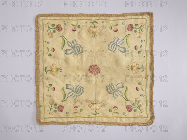 Church napkin, Church paraments; flowers; leaves; plant ornaments; sacred art. Napkin of white silk fabric embroidered with single projections of large flowers and fruit. Trimmed with silk braid with short shreds. Plain weave fabric, density 34 weft × 34 warp threads per cm, two workshop edges preserved, piece width 45 cm. Flat, pierced embroidery with colored silk threads — a thread of one color penetrates a row of threads of another color creating shaded transitions. Embroidery with gold thread around petals of peonies, irises, and tulips. Colors subdued but not faded: burgundy, multiple blues, cream, beige, ochre, green, light yellow-green, gold. Compared to a related napkin, colors are less bright and embroidery more detailed; napkin also appears earlier. Early 18th century, Poland. Height 42.5 cm, width 45 cm., A square textile with a fringe border in a golden brown color lies flat against a light gray background; the central field of the textile is a pale beige or cream tone embr...