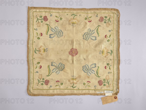 Napkin of white silk fabric embroidered with a pattern of single projections of large flowers and fruit. Trimmed with silk braid with short shreds. Plain weave fabric, density: 34 weft threads and 34 warp threads per 1 cm, two workshop edges preserved, piece width: 45 cm. Flat, pierced embroidery with colored silk threads - a thread of one color penetrates a row of threads of another color, thus shading the color transitions. Embroidery with gold thread around the petals of peonies, irises, and tulips. The colors are subdued, but not faded: burgundy, blue in several tones, cream, beige, ochre, green, light yellow-green, gold. Compared to another napkin, the colors of the silk threads are not as bright, and the embroidery is more detailed; the napkin also seems to be earlier. Early 18th century, Poland. Height 42.5 cm, width 45 cm., A square fabric square with a beige background and a fringed tan border, decorated with embroidered floral motifs in colors including blue, green, pink, yel...