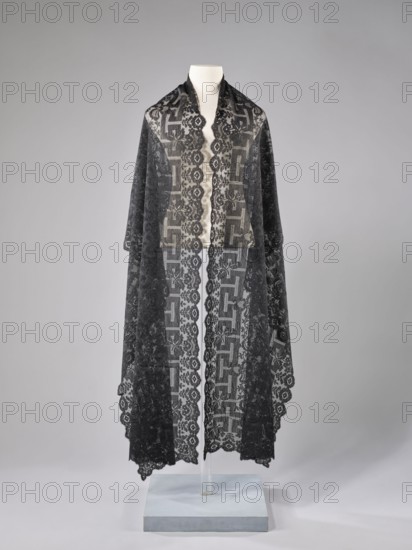 Shawl; maker, shawl; fashion; women's clothing; clothing accessory; floral ornaments; meander ornament. The meander is associated with straight flower branches with a single large flower directed towards the outer edge. The outer edge is serrated. 1st half of the 19th century, France. Lace. Length 270 cm; width 63.5 cm., A mannequin torso draped with a long, sheer lace shawl featuring intricate floral and geometric patterns, displayed against a smooth light gray background and mounted on a pale bluish-gray square base; the visible colors are black on the lace, cream on the mannequin torso, pale bluish-gray on the base, and various tones of gray in the background.