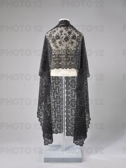 Shawl, shawl; 1st half of the 19th century, France; women's clothing; clothing accessory; floral ornaments with meander motif — the meander is associated with straight flower branches with a single large flower directed towards the outer edge; outer edge serrated; lace; length 270 cm; width 63.5 cm; provenance: purchase., A mannequin draped in a long, sheer lace garment with floral and geometric patterns, shown from the back against a neutral backdrop; the lace is dark and contrasts with a light underlayer around the shoulders and waist, and the garment falls into scalloped edges with decorative motifs; the base and support are visible beneath the fabric and the background is a smooth gradient of pale gray.
