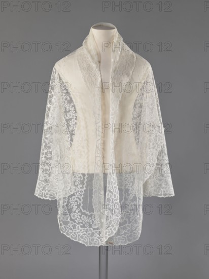 Cape, lace, clothing accessory for women's fashion, 19th century, Europe; length 75 cm, width 192.5 cm., A mannequin torso draped with a sheer lace shawl in shades of white and ivory against a neutral grey background; the shawl has a delicate floral and scrollwork pattern with scalloped edges, long panels hanging down the front and over the shoulders, and semi-transparent areas revealing the smooth fabric of the mannequin beneath; the overall colors visible are white, ivory, grey, and subtle off-white tones.