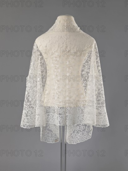 Cape, lace, clothing accessory, women's clothing, fashion, capes, 19th century, Europe, length 75 cm, width 192.5 cm, A mannequin draped with a delicate lace shawl or cape shown from the back, featuring sheer floral lace panels in off-white and cream over a solid cream underlayer; the lace has intricate swirling and floral embroidery with scalloped edges, and the garment has a raised collar in matching cream; the background is a flat medium gray.