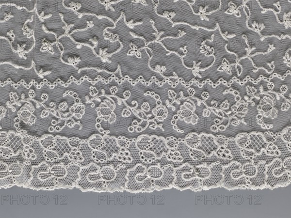 Cape, lace, clothing accessories, women's clothing, fashion, capes, 19th century, Europe, length 75 cm, width 192.5 cm, A section of delicate lace fabric fills the image, showing a layered arrangement of embroidered patterns on a fine net background. The lace displays floral and vine motifs with looping stems and small stylized blossoms, arranged in horizontal bands separated by scalloped or wavy linear borders. The fabric appears in shades of off-white and cream against a muted gray backdrop, with the off-white embroidery standing out against the darker gray net. The lower edge shows a denser scalloped lace trim with rounded motifs, while the upper areas feature more open netting with smaller floral and foliate elements. The overall texture is intricate and airy, with visible tiny hexagonal netting between the embroidered designs.