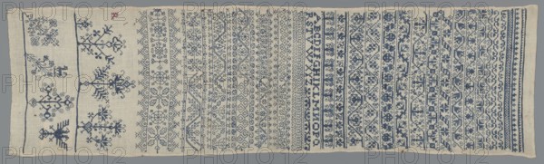 Embroidery sampler, Sampler with a cross-stitch pattern of trails, flower bushes, and letters. Blue embroidery on white canvas. Bands of geometric and floral ornaments with geometrized twigs and leaves; one edge with several larger stylized flower-bush motifs. In the corner, the silhouette of a double-headed eagle. Between the bands, beside various geometrical flower tendrils, a double Holbein-stitch ornament. 17th century, Silesia. Embroidery on fabric; height 81.5 cm, width 23 cm., A rectangular piece of fabric lying flat with a background color of off-white or beige and detailed embroidery in shades of blue and a small spot of red, showing a series of horizontal bands across its width. The left side has a few larger, more open motifs including stylized plant- or tree-like shapes and geometric forms separated by narrow vertical stitched lines, while the rest of the surface is filled with several tightly packed horizontal bands of repeating ornamental patterns such as floral motifs, i...