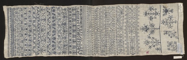 Embroidery sampler, Sampler with a cross-stitch pattern of trails, flower bushes, and letters. Blue embroidery on white canvas. Geometric and floral ornaments with geometrized twigs and leaves; several larger motifs along one edge in the form of stylized flower bushes. Corner features the silhouette of a double-headed eagle. Between the paths, next to geometrical flower tendrils of various types, is a double Holbein stitch ornament. 17th century, Silesia. Embroidery on fabric; height 81.5 cm, width 23 cm., A long rectangular piece of fabric laid flat showing a dense array of horizontal embroidered bands and motifs. The fabric is a light beige or off-white and the embroidery is primarily a dark blue, with a small area of red stitching near one edge. On one side there are several narrow borders with repeating geometric and floral motifs, while the central area contains rows of varied ornamental patterns including stylized flowers, vines, and abstract shapes worked in the dark blue thread...