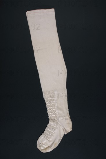 Stockings; unknown creator; stockings; purchase provenance; underwear; fashion; clothing accessories; women's accessories; miscellaneous; knitted goods; knitwear; women's fashion; ca. mid-19th century; Europe; clothing; length 57 cm, A single long stocking laid flat against a dark background, predominantly off-white or cream in color with a narrow band of pale pink along the top edge; the stocking shows a smooth plain upper leg section transitioning to an area of decorative textured stitching and lace-like patterns along the lower leg and instep in matching cream tones, with a shaped heel and rounded toe area and visible seam lines and subtle fabric creases.