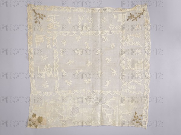 Tablecloth. Embroidered tablecloth; white embroidery on white mesh with gold-thread accents in stitched stitches. Central motifs of small floral sprigs. Three edges feature motifs of trees and houses; the fourth, widest edge has a wide twig motif. Corners show four different floral or leafy sprigs. 18th century, Poland. Materials: fabrics. Dimensions: height 65 cm, width 66 cm., Function: church parament / sacred art church furnishings., A square piece of lace fabric lies flat against a pale gray background, showing an overall cream color with a few tan and brown embroidered accents at two corners. The lace has a scalloped border and an inner rectangular frame, both in cream, with a delicate netted pattern filling the central area. Scattered throughout the central field are several small floral motifs in cream, and larger floral and leafy designs appear near the edges and corners. The lower area features a denser arrangement of lace patterns with overlapping leaves and textured netting...