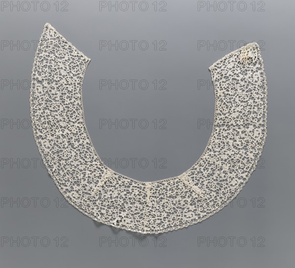 Collar, floral ornaments, semicircular shape obtained using darts with elongated corners, de brides type background with picots; lace, clothing accessory; 17th/18th century, Italy; width 15 cm, length 150 cm., A delicate semicircular lace collar with an open center displayed against a smooth background; the collar is made of fine crocheted or tatted lace forming a repeating network of small connected loops and floral-like motifs, with scalloped outer edges and slightly irregular inner edges. The lace appears off-white or cream in color, and the background is a uniform medium gray. The texture of the lace looks lightweight and airy, casting faint soft shadows on the background.