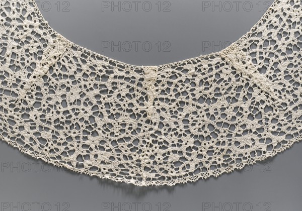 Collar, floral ornaments, semicircular shape obtained using darts with elongated corners, de brides type background with picots, lace collar, fashion accessory; 17th–18th century, Italy; lace; width 15 cm, length 150 cm., A close-up view of a delicate lace collar displayed against a smooth background, showing an intricate openwork pattern of interconnected loops and floral-like motifs in a cream or off-white color, with the backdrop appearing as a muted gray; the lace edges are scalloped with threads and tiny picot details, and the texture shows fine threadwork and slight shadows where the lace lifts from the background.