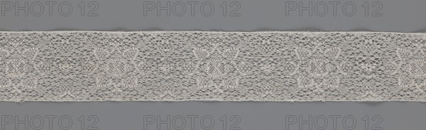 Fragment of bobbin lace, 18th century, Flanders, lace, width 9 cm, length 51 cm, A horizontal strip of delicate lace with an open, airy weave stretches across a gray background; the lace is an off-white or cream color with an intricate repeating pattern that includes round floral motifs and scalloped edges, and the background shows varying shades of medium gray that contrast with the lighter lace.