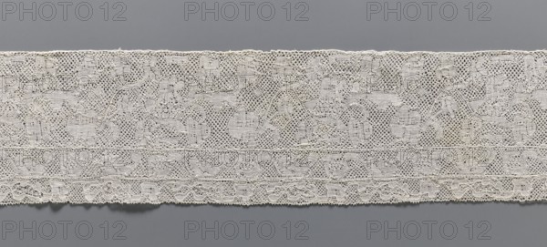 Lace fragment, bobbin lace Binche lace, 18th century. Background: mesh with large, rounded meshes. Edges of motifs uncontoured. Large, narrow laces are sewn on at the bottom edge; the wider one has a motif of flower branches arranged in a twig; the other, narrower one, has a motif of a flower tendril. Width 12 cm, length 61 cm., A horizontal strip of lace displayed against a solid background, showing a delicate openwork pattern with a floral and scroll motif. The lace appears in shades of off-white and cream with subtle variations in tone, and the background behind and below the lace is a smooth gray. The lace has a scalloped lower edge and a slightly uneven upper edge, with a few rows of denser woven bands running parallel to the edges. The overall texture is intricate and airy, with small holes and looping threads forming repeating decorative shapes.