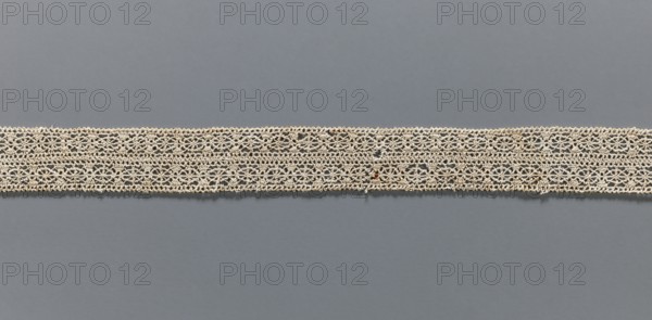 Fragment of needle lace, 16th–17th century, Flanders; width 2.8 cm, length 55 cm; provenance: Henryków Heinrichau;, A horizontal band of delicate lace runs across the middle of the image against a smooth background; the lace is a light beige color with an open, intricate pattern of interlocking loops and small floral-like motifs, and the background is a muted bluish-gray.