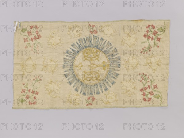 Antependium, antependium. Fragment of church embroidery. On cream silk satin 46 gauge, green selvedges with embroidery and glued appliqué of colorful silk threads, gold and silver threads, and sequins. In the center, in a large radiant medallion, is the IHS monogram with a cross and three nails. The background is filled with projections of stylized floral sprigs. Small sprigs in the corners and on the sides of the medallion are embroidered; the remaining background motifs are appliquéd glued. 18th century, Poland. Fabric; height 82 cm, width 47 cm., A rectangular piece of pale beige fabric with a large circular embroidered motif near the center featuring a radiating sunburst of blue stitches around a central round area filled with yellow-gold embroidery; scattered around the central motif are several floral and scrollwork embroidered designs in yellow-gold, with clusters of small red flowers and green stems and leaves appearing along the left and right edges and in a few interior spots...