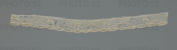Lace fragment, needle-stitched lace, highly elongated openwork ovals. Above the edge ornament, against a mesh background, a winding line interrupted by openwork circles; in the bends of the line, a rather large three-leafed branch projection. 18th century, France, width 3.5 cm, length 42.5 cm., Repossession, A long narrow strip of lace displayed horizontally against a gray background, the lace is off-white to cream in color with a fine netted ground and a scalloped lower edge; a decorative pattern of interconnected loops and braided lines runs along the length, with small floral and leaf motifs interspersed above the main border, and there are a few irregular holes and slight fraying along the top edge.