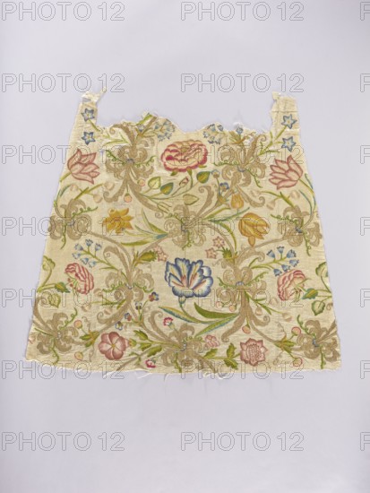 Two fragments of a dalmatic, embroidery on silk fabric interwoven with silver thread, front and back. Embroidered floral tendril with tulips, bellflowers, pansies, carnations, daffodils, irises, and roses with species-specific leaves, plus golden fantastic flowers with bent stems. Predominant colors: yellow several shades, blue, pink, red, green, and gold. Embroidery: metal thread gilded silver plate woven on a silk base and multicolored silk; gold embroidery with laid flat stitch, metal threads held with silk yarn; silk embroidery with satin and split stitches. Fabric: silver lamé grosgrain interwoven with silver thread, gauge width 50.5, yellow-red selvedge, density 17–18 weft threads/cm², 14–15 warp threads/cm². Dating: 18th century embroidery, 16th century fabric. Place of origin: Poland embroidery, Italy fabric. Liturgical vestment. Dimensions: length 104.5 cm, width 87 cm., A rectangular piece of fabric with a scalloped top edge and frayed bottom edge lies flat against a pale lav...