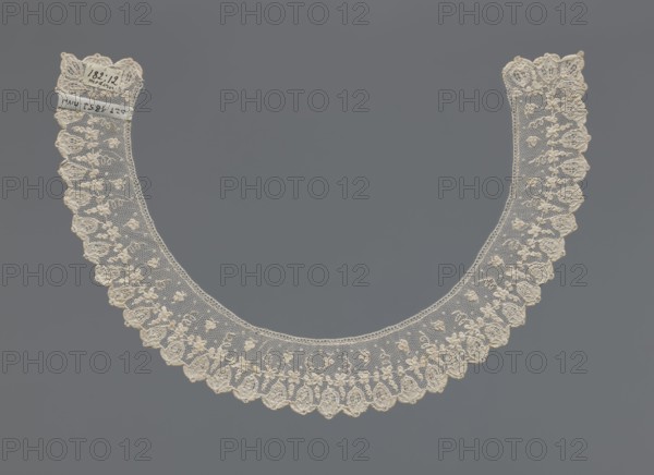 Collar, Repossession, Women's clothing accessory, lace, 19th century, possibly France. The collar is a band of equal width, arched, with a floral ornament set against a mesh background. Along the rim runs a row of flower calyxes branching from a continuous branch decorated with small quatrefoils. Dimensions: width 3.5 cm, length 46 cm., A delicate semicircular lace collar in off-white with a fine net background and a scalloped outer edge, featuring embroidered floral motifs and raised decorative stitching along the outer border, laid flat against a solid medium-gray background.