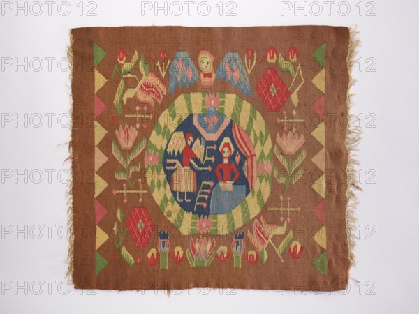 Ornamental-figural tapestry, flowers, floral ornaments, angels, Copernicus, Mary mother of Jesus Christ, Annunciation Bible; New Testament, furniture upholstery, interior furnishings, weaving, tapestries. In the central medallion are the Virgin Mary and an angel. Outside the medallion are flower branches, heads, and other decorations. The ornament is strongly stylized and geometric. Without a border. Colors: light brown, navy blue, red, yellow, blue, and green. 18th century, Norway. Fabrics; height 59 cm, width 62 cm., A rectangular woven textile with fringed short edges displays a central circular medallion with a dark blue interior containing stylized human figures and geometric shapes, surrounded by a green and pale yellow checker border; the field around the medallion is a warm brown and features symmetrical floral and geometric motifs in red, pink, green, pale yellow, and blue, with a repeating triangular border pattern along the left and right edges and frayed threads visible at ...