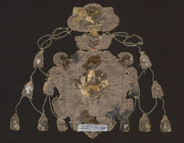 Coat of arms, embroidery, provenance message: Vasas family; coats of arms: Vasa sheaf on central shield. In four fields: 1 Eagle with a crown — Polish; 2 Three crowns — Swedish; 3 Pogon — Lithuanian; 4 Gryf — Ruthenian. Shield topped with a crown and a bishop's hat. Possible owners: John Albert Snopek coat of arms, Bishop of Kraków, cardinal, died 1634; Jan Kazimierz Snopek coat of arms, elected King of Poland 1648, abdicated 1668, titular cardinal; or Ferdynand Vasa, brother of Jan Kazimierz. Embroidery background: linen canvas with silk satin in red and blue applied to canvas. Embroidery on a backing of various heights made of linen threads. Flat and convex embroidery with metal threads: silver and gold plate braided on silk yarn; drawn wire in silver and gold; bullions of drawn wire and narrow gold plate. Silk embroidery in satin and knot stitch. Attributed to E. Soszko; ca. 17th century, Poland. Materials: fabrics; height 16 cm., An irregularly shaped, worn textile or paper object ...