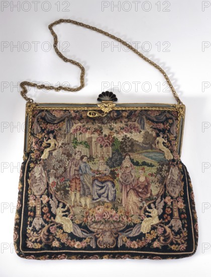 Women's handbag. Handbag in the shape of a rectangle, slightly narrowed at the top. Embroidered with colorful silks on canvas using the petit point stitch. Embroidery with a court scene in historical costume in a park landscape covers both sides. The scenes are framed by curtains and floral garlands on all four sides, supported by figures at the bottom, two angels at the top, a woman. Black lacquered brass frame with applied gilded or glazed decoration in the form of small volutes placed in the corners of the frame and at the base of the fan-shaped lock placed in the center of the frame. Gold-colored metal chain handle. Light beige grosgrain lining with a pocket. Genre scenes in a landscape, park scenes, court scenes, garlands ornament. Attributed to Austria, dated 1915–1930. Dimensions: height 15 cm, width 17.5 cm., A decorative handbag with a metal frame and a chain strap is shown against a white background; the frame is gold-toned with an ornate clasp topped by a black fan-shaped ac...