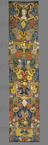 Tapestry embroidered in wool and silk on linen canvas. In the upper part, within a decorative cartouche, is the bust of a lady, her face framed by curls forming a hairstyle. Around it are dense scrolls of large leaves, flowers, and fruit. Unedged. Vivid colors: brown background, green, pink, red, blue, sapphire, and yellow ornament. The plant motifs of the nine fabrics comprising this set do not differ from each other. Stylized leaves, flowers, and fruit fill the entire surface of the panel. The composition unfolds on both sides of the axis, defining a symmetrical division of the decoration, similar to the large-pattern silk upholstery fabrics fashionable in the late 17th and early 18th centuries. Minor differences include the inclusion of small animal silhouettes on some of them, which enrich the decoration. All fabrics are decorated with the same fruit: plump bunches of black and white grapes, yellow apples, and dark red cherries. Vivid colors, brown background, shaded ornament: pink...