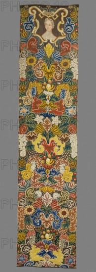 Tapestry. Tapestry embroidered in wool and silk on linen canvas. In the upper part, in a decorative cartouche, is the bust of a woman with two red flowers pinned in her hair. Around it are dense scrolls of large leaves, flowers, and fruit. Unedged. Vivid colors: brown background, red, pink, green, sapphire blue, yellow, olive, and ochre ornament. The plant motifs of the nine fabrics comprising this set do not differ from each other. Stylized leaves, flowers, and fruit fill the entire surface of the panel. The composition unfolds on both sides of the axis, defining a symmetrical division of the decoration, similar to the large-pattern silk upholstery fabrics fashionable in the late 17th and early 18th centuries. Minor differences include the inclusion of small animal silhouettes on some panels, which enrich the decoration. All fabrics are decorated with the same fruit: plump bunches of black and white grapes, yellow apples, and dark red cherries. Vivid colors, brown background, shaded o...