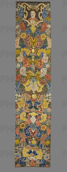 Tapestry. Tapestry embroidered in wool and silk on linen canvas. In the upper part, within a decorative cartouche, is the bust of a nobleman with a mustache and shaved hair, wearing a zupan and delia. Around it are dense scrolls of large leaves, flowers, and fruit. Among them, a falcon is depicted in the center. No border. Vivid colors: brown background, ochre ornament, pink, green, blue, sapphire, red. The plant motifs of the nine fabrics comprising this set do not differ from each other. Stylized leaves, flowers, and fruit fill the entire surface of the panel. The composition unfolds on both sides of the axis, defining a symmetrical division of the decoration, similar to the large-pattern silk upholstery fabrics fashionable in the late 17th and early 18th centuries. Minor differences include the inclusion of small animal silhouettes on some of them, which enrich the decoration. All fabrics are decorated with the same fruit: plump bunches of black and white grapes, yellow apples, and ...
