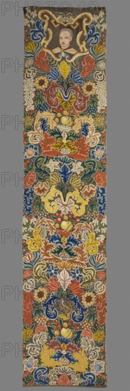 Tapestry, Tapestry embroidered in wool and silk on linen canvas. In the upper part, within a decorative cartouche, is the bust of a nobleman in zupan and delia, with a mustache and shaved hair. Around it are dense scrolls of large leaves, flowers, and fruit. Among them, in the lower part, the figure of a bird. No border. Vivid colors: brown background, blue, sapphire, green, ochre, beige, red, pink ornament. The plant motifs of the nine fabrics comprising this set do not differ from each other. Stylized leaves, flowers, and fruit fill the entire surface of the panel. The composition unfolds on both sides of the axis, defining a symmetrical division of the decoration, similar to the large-pattern silk upholstery fabrics fashionable in the late 17th and early 18th centuries. Minor differences include the inclusion of small animal silhouettes on some panels. All fabrics are decorated with the same fruit: plump bunches of black and white grapes, yellow apples, and dark red cherries. Vivid ...