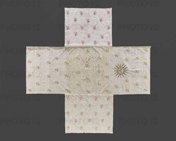 Church napkin. Thin white linen sewn from five rectangular pieces in the shape of a cross. Embroidered with evenly spaced projections of stylized floral sprigs in gold, dark pink, and straw. One side rectangle bears an embroidered gold IHS monogram within a halo. On the opposite rectangle, on the edge, is the inscription: ANNA Z RUSOCKICH ORZECHOWSKA. R. 1743. 1743. Poland. Fabrics. Height 290 cm, width 290 cm. Creator: Anna Orzechowska née Rusocka 18th century; fl. ca. 1743. Function: church paraments / church napkin; imagery: flowers, leaves, plant ornaments; sacred art., A textile arranged in a cross shape lies flat against a dark gray background, consisting of a central rectangular panel with extensions at the top, bottom, left, and right. The fabric is predominantly off-white to cream with visible wrinkles and a few small spots and stains, and it is patterned with a repeated floral motif in light beige and pale brown across most panels. The top panel shows a repeating small floral...