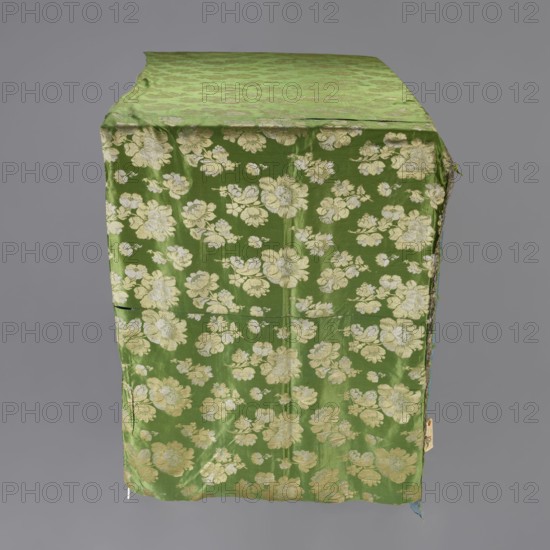 Church napkin, creator, ; church paraments; evangelical church furnishings; Sielec Swietokrzyskie Voivodeship, Staszów County; flowers, leaves, plant ornaments; sacred art; churches and chapels furnishings; 17th century, Italy; fabric; height 120 cm, width 62 cm, A length of green fabric with a repeating floral pattern in pale yellow and off-white draped over a rectangular form against a neutral gray background, showing a top surface and a hanging front panel with a few creases and slight fraying at one edge.