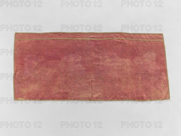 Church napkin, gift, church paraments, evangelical churches furnishings, Sielec Swietokrzyskie Voivodeship, Staszów County, evangelical church Sielec - furnishings; motif: flowers, leaves, plant ornaments; sacred art; churches and chapels furnishings; date: 1700–1730; origin: France; material: fabrics; dimensions: height 97 cm, width 216 cm, depth 10 cm., A rectangular fabric laid flat against a light gray background, primarily a faded reddish color with areas of muted pink, peach, and tan showing through; the fabric has visible creases and a slightly wrinkled texture, and a narrow decorative trim in a goldish color runs along the edges.