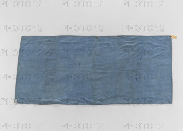 Church napkin; creator, ; church paraments; evangelical churches furnishings; Sielec Swietokrzyskie Voivodeship, Staszów County; evangelical church Sielec — furnishings; decoration: flowers, leaves, plant ornaments; sacred art; churches and chapels furnishings; dated 1700–1730; origin: France; material: fabric; dimensions: height 97 cm, width 216 cm, depth 10 cm., A rectangular piece of fabric laid flat against a light gray background, appearing blue with variations in shade and subtle darker and lighter patches, showing visible creases and folds across its surface, with a hemmed edge and a group of small round metal eyelets along the top edge, a few tiny darker spots and minor imperfections scattered on the cloth, and small fabric tabs at the corners.