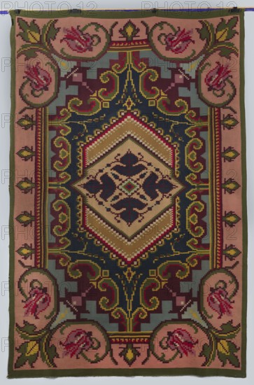 Kilim, decorative flatwoven textile, 19th/20th century, Kosów; manor and house furnishing; decorative fabric; height 304 cm, width 202 cm., A rectangular woven textile with a central diamond-shaped medallion surrounded by ornate geometric and floral motifs in a palette of deep navy, olive green, muted pink, mustard, burgundy, beige, and pale blue-gray. The central area features layered chevron bands in beige and mustard framing a dark navy inner diamond with symmetrical stylized leaf shapes in burgundy and navy. Around the medallion are scrolling arabesque forms and stepped geometric blocks in olive, mustard, burgundy, navy, and blue-gray. The border consists of a muted pink field with repeating roundels containing stylized floral forms in shades of pink and burgundy, linked by olive green foliage and framed by narrow bands of olive and mustard. The overall appearance is richly patterned with pixelated, tapestry-like stitching and contrasting color edges.