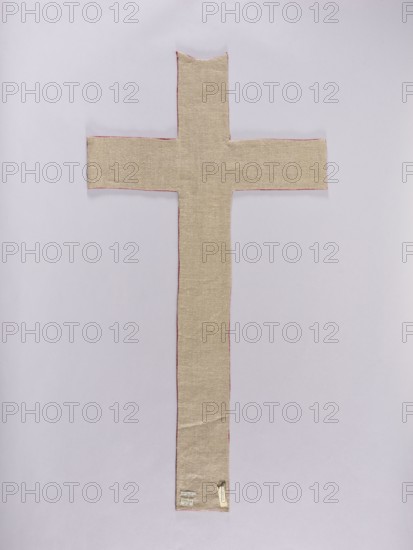 Chasuble pillar, embroidery, ; subject: Christ Crucified; function: liturgical vestment church paraments; iconography includes flowers, leaves, plant ornaments; sacred art; 16th/17th century, Poland. The chasuble is shaped in the form of a cross with arms slightly tilted upwards, made of silk rep fabric. The fabric features an applied cross with Christ and eight rosettes; the ends of the cross's arms are half-rosettes. Embroidery on linen canvas applied with metal thread silver and gold plate woven onto a silk base, metal threads couched with silk yarn; silk yarn embroidery with flat and split stitches. Materials: fabrics; dimensions: length 106 cm, width 55 cm., A vertically oriented cross-shaped fabric piece lies flat against a pale background; the fabric is a beige or light tan color with a visible woven texture and narrow reddish edges, and a small rectangular tag is attached near the lower end.