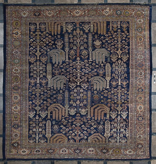 Carpet, The main field is filled with motifs of various species of trees arranged in three vertical rows; between the trees are flower bushes, palmettes, and small rosettes. Seven-strip border with plant ornament. Colors: navy blue, red, yellow, cream, navy blue, blue and red. A similar carpet contains in the central field a section of a similar garden 1/4 with almost identical motifs in reversed colors, dark brown with a navy blue outline on a sandy background. Dated to the 18th century and knotted in northwestern Persia Kurdistan. Cotton warp, S7Z; symmetrical Z2S wool knots, density approx. H27 x W26 ˜702 knots/dm2. Rectangular section contains stylized weeping willows, cypresses, flowering trees pomegranate, lotus palmettes. 19th century, Iran. Height 512 cm, width 430 cm., A rectangular woven rug with a dark blue field densely patterned with a repeating botanical motif featuring stylized trees, branches, and floral forms in shades of beige, cream, tan, muted gold, and light blue, ...