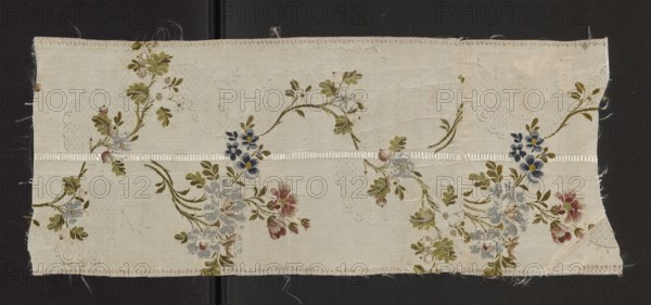 Fragment of silk fabric, patterned brocade, 18th century France. Floral design with dark and light orange roses, light and dark blues, celadon and olive greens, silver, orange, and yellow on a white background. Grosgrain weave with weft texture liseré. Height 53 cm, width 21 cm. Creator and provenance unknown., A rectangular fabric sample laid flat against a dark background shows a light cream base with a floral pattern in muted colors; a few clusters of flowers in shades of dusty blue, muted red, soft pink, and deep navy are connected by winding olive and moss green stems and leaves, with small touches of pale yellow at some flower centers. A horizontal ribbon-like band of slightly shinier cream runs across the middle, and there are faint textured or lace-like woven areas in the same cream tone that form subtle oval and scalloped shapes behind the floral motifs. The fabric edges are slightly frayed, and the overall surface shows fine woven threads and a gentle sheen.