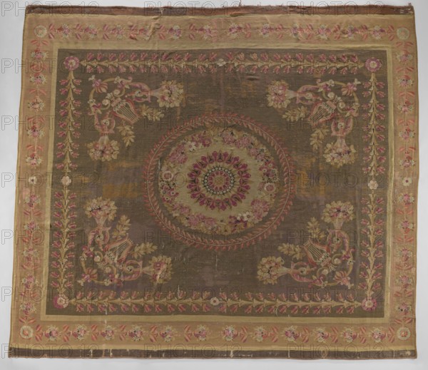 Ornamental tapestry, Late 18th century, Flanders. This ceiling floor tapestry has symmetrical decoration: a central rosette surrounded by two floral and leafy wreaths; corner compositions of horns filled with flowers, lyres, and intertwined acanthus leaves; overall frame of leaves and rosettes. Border repeats leaves, rosettes, and flowers. Colors: cream, olive, and sand background with pink, green, and blue ornament. Materials: woven fabrics. Dimensions: height 517 cm, width 460 cm., A large rectangular textile with a central circular medallion surrounded by floral motifs and ornate corner decorations, featuring a background of muted brown and ochre tones with accents of pink, rose, green, gold, and cream; a broad border in a lighter tan or beige frames the piece, decorated with repeated floral garlands in pink and green, and inner narrow bands in gold; the central medallion has concentric floral patterns in rose, pink, cream, and green, and is encircled by a wreath-like design in redd...