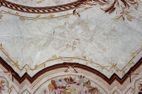 A so-called ceiling tapestry, tapestries, fabrics, tapestries, fabrics, knotted monograms, floral motifs, interior furnishings, weaving. In the center, a rosette surrounded by a floral wreath. Surrounded by rectangular frames with rounded shorter sides and floral garlands. In the corners are medallions with a knotted CKJ monogram. The border varies in color with plant patterns imitating the damask technique. Colors: pink, red, light brown, and olive. Early 19th century, France; height 681 cm, width 385 cm., A decorative textile with a pale beige background featuring a central faint botanical motif in very light beige and off-white tones, surrounded by ornate curved borders in shades of brown and tan with leaf-like accents in muted yellow and gold; the lower edge shows a floral arrangement in soft pinks, muted reds, pale blues, cream, and yellow with greenish-brown leaves, and there are stylized zigzag bands and ribbon-like patterns in dark brown, tan, and cream.