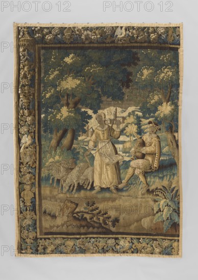 Figural tapestry, flowers, sheep, trees, bagpipes, landscapes, buildings, borders, folk musical instruments, tapestries, hills, interior furnishings, interior decorations, scenes with a landscape background, pastoral and rural scenes, spindles, allegorical scenes. Most of the fabric preserved, missing the right border. In the center, against a forest landscape, a shepherd plays bagpipes while a shepherdess stands with a distaff; sheep graze around them. Border with motifs of flowers, birds, and vases. Colors: blue, sand, brown, green, beige. 17th–18th century, Flanders. Materials: fabrics. Height 281 cm, width 200 cm., A woven textile depicting a pastoral scene framed by an ornate border, with dominant colors of blue, green, beige, brown, and touches of gold; within the scene a woman in a long beige dress and apron stands holding a staff while a seated man in a beige and brown outfit with decorative elements holds a stringed instrument, a few sheep graze nearby on grassy ground, and a ...