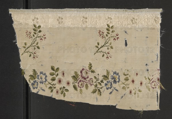 Fabric fragment, fabrics, fragments of silk patterned fabric with preserved selvedge, 18th-century silk, Louis XV/16th style. Materials: silk brocade with grosgrain weave; colors include celadon-green, light grass green, pale yellow, sky blue, blue, white, brick-red/rust, raspberry-whitened, pale pink on white and cream background with white warp stripes. Dimensions: height 14.8 cm reported, overall height 30 cm, width 20 cm. Date/place: 2nd half of the 18th century, France. Selected edge width: 0.6., A rectangular piece of fabric with frayed edges laid on a dark background, featuring a pale beige ground and a textured cream band along the top; the fabric shows areas of wear and small irregular holes. Scattered floral motifs embroidered or printed in olive green leaves with small red buds appear across the central area, and a border of larger floral clusters runs near the lower edge with flowers in dusty blue, muted rose, and faded purple accompanied by olive green foliage. There are s...