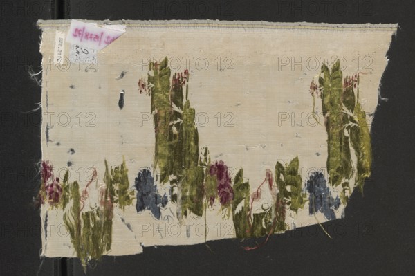 Fabric fragment, fragments of silk fabrics, patterned fabrics, fabrics with preserved selvedge, 18th-century silk fabrics, Louis XV/16th style. Materials: silk; weave: grosgrain; colors: white and cream background with white warp stripes; brocade in celadon-green, light grass green, pale yellow, sky blue, blue, white, brick-red/rust, raspberry-whitened, pale pink. Selected edge width: 0.6 cm. Dimensions: height 14.8 cm; overall height 30 cm, width 20 cm. Date/place: 2nd half of the 18th century, France., A worn rectangular fabric fragment with a beige background mounted on a dark surface, showing frayed edges and small areas of damage; a few vertical and irregular green shapes resembling plant forms run across the lower half and rise toward the middle, interspersed with patches of blue and purple fibers and thin red threads; the beige weave shows darker worn spots and small holes, and the top edge has a narrow stitched border in light tones; overall colors visible include beige, green,...