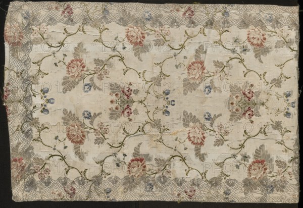 Fragment of a fabric in the form of a tapestry or napkin;, Fragment of 18th-century French silk fabric with White grosgrain Gros de Tours background enriched with small brocaded ornament liseré in colorful threads. Pattern brocaded with gold, pale pink to red, grass green, sky blue, dark blue, burgundy-pink. Preserved selvedge, fabric width and pattern. Dimensions: 86 cm height; piece width 54.5 cm reported 32.5 x 53; border widths 0.4 + 0.3 cm., A rectangular piece of fabric with a pale beige background covered in a floral pattern featuring a few large roses in muted pink and red, several smaller flowers in blue and light pink, and many leaves in soft gray and olive green connected by winding olive green stems, the surface showing areas of worn texture and slight fraying, and a scalloped lace-like border in gray with occasional touches of red and blue along the edges.