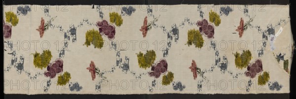 Fabric fragment, silk, Krzeszowice Lesser Poland Voivodeship, 18th century, possibly England. Fragment of white grosgrain silk with a small liseré sub-pattern and a colorful floral brocade in threads of white, light blue, blue, dark blue, dark pink, cherry red, apricot, and pale red. Sub-pattern: net-like with small motifs; composed of two intersecting winding ribbons of tiny blue flowers, one intersected by multi-tiered bouquets of various flowers in blue, plum, and yellow-green. Fabrics with preserved selvedge. Reported dimensions: height 33 cm other width, also recorded height 106 cm x width 27 cm., A rectangular piece of fabric with a pale cream background patterned with a repeating ogee-like chain of abstract shapes in muted blue, punctuated by scattered floral-like blotches in olive green, deep mauve, and dusty rose; the fabric shows a folded corner at one end and a few small crease lines and slight surface wear, with the pattern appearing slightly faded in places.