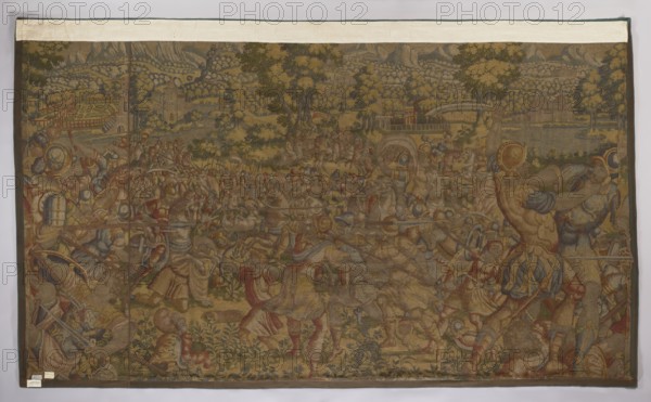 Figural tapestry by Franz Geubels 1535–1590, 2nd half of the 16th century, Flanders Brussels. Woven wool and silk, height 218 cm, width 358 cm. Depicts fighting soldiers in the foreground and background with figures of a woman and a man facing each other, figures in military costume, decorative fabrics and interior furnishings, and a mountain landscape in the background. No border. Colors: green, red, sapphire blue, sand, and yellow., A large woven tapestry depicting a crowded outdoor scene with many human figures and horses spread across a landscape of trees and distant hills, rendered in muted tones of brown, tan, olive green, and faded gold with touches of red, blue, and gray; the foreground shows dynamic poses of armored and robed figures, some raising weapons and shields, others fallen or kneeling, while a group of horses and riders appear amid the action; midground and background contain clustered trees, a few structures, and a bridge-like element, with layered foliage creating d...
