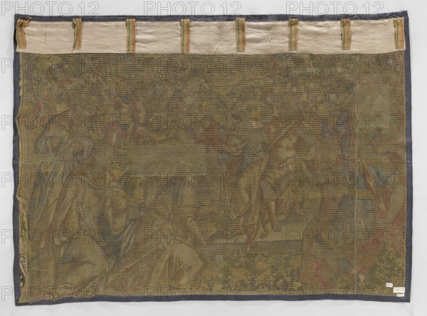 Figural tapestry, Geubels, Franz 1535–1590 maker/workshop, battle scene depicting a victorious commander wearing a laurel crown seated on a dais surrounded by soldiers; in the foreground a kneeling group of delegates from a defeated city—one kneeling soldier points to the keys held by the lead delegate; men on wheels present keys to the leader; in the background an approaching army on horseback, city walls and gardens visible between trees, high horizon partially obscured by trees and mountains. No border border clipped in one variant. Limited, saturated palette; predominant colors green, red, sapphire also sand and yellow. Materials: tapestry decorative fabric, interior furnishing. Date: 2nd half of the 16th century. Origin: Flanders, Brussels. Dimensions: height 218 cm, width 295 cm., A large rectangular textile viewed from the back with a coarse mesh net overlaying a faded woven scene, bordered by a dark gray fabric trim; the top edge shows a lighter beige strip with several hanging...