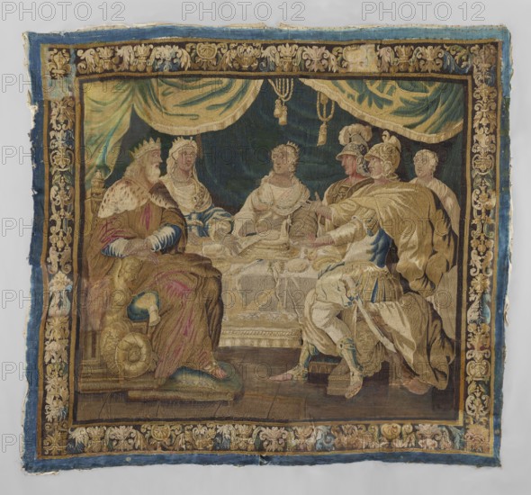 Figural tapestry, provenance, subject: royal feast — around a table under hanging draperies sit a king and queen in crowns on the left, a young crowned woman in the center, and on the right two men in armor with a servant behind them. On the table, a peacock platter among the tableware. Border with motifs of vases of leaves and palmettes and floral ornaments. Features flowers; decorative fabric for interior furnishings. Materials: woven fabrics; colors: ochre brown, green, and blue. 17th century, Flanders. Dimensions: height 268 cm, width 300 cm., A woven scene shows a group of people seated around a table beneath draped curtains, with a decorative border framing the image; colors visible include shades of blue, gold, beige, brown, green, cream, and touches of pink and red. The left side depicts a crowned figure wearing fur-trimmed robes and seated on a cushioned seat, next to a woman in a light-colored gown and jewelry; at the center sits another crowned person in a pale dress. To the...