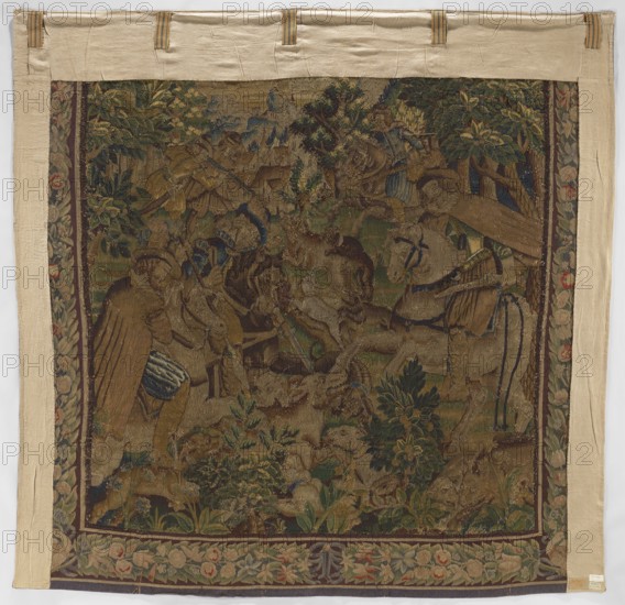 Figural tapestry, Scene: in the foreground at the edge of a forest, among low vegetation, dogs attack a wild boar; above, horseback riders with sabers or rifles; in the distance, urban buildings and a castle on a hill. Border with a motif of densely interwoven flowers and leaves. Motifs: flowers, floral ornaments, dogs, hunting, hunters, trees, horseman, forests, weapons., woven tapestry, decorative fabric; colors: brown, green, beige, red, gray. Date: 2nd half of the 17th century. Place of origin: Flanders. Dimensions: height 287 cm, width 291 cm., A rectangular woven tapestry with a wide beige fabric border and a central scene depicting a wooded outdoor setting in muted greens, browns, blues, and golds; within the scene a group of human figures and animals are arranged among dense foliage, trees, and flowering plants, with a few figures wearing garments in shades of brown and blue and a few animals showing beige and brown tones; the tapestry has a decorative floral border in green, p...